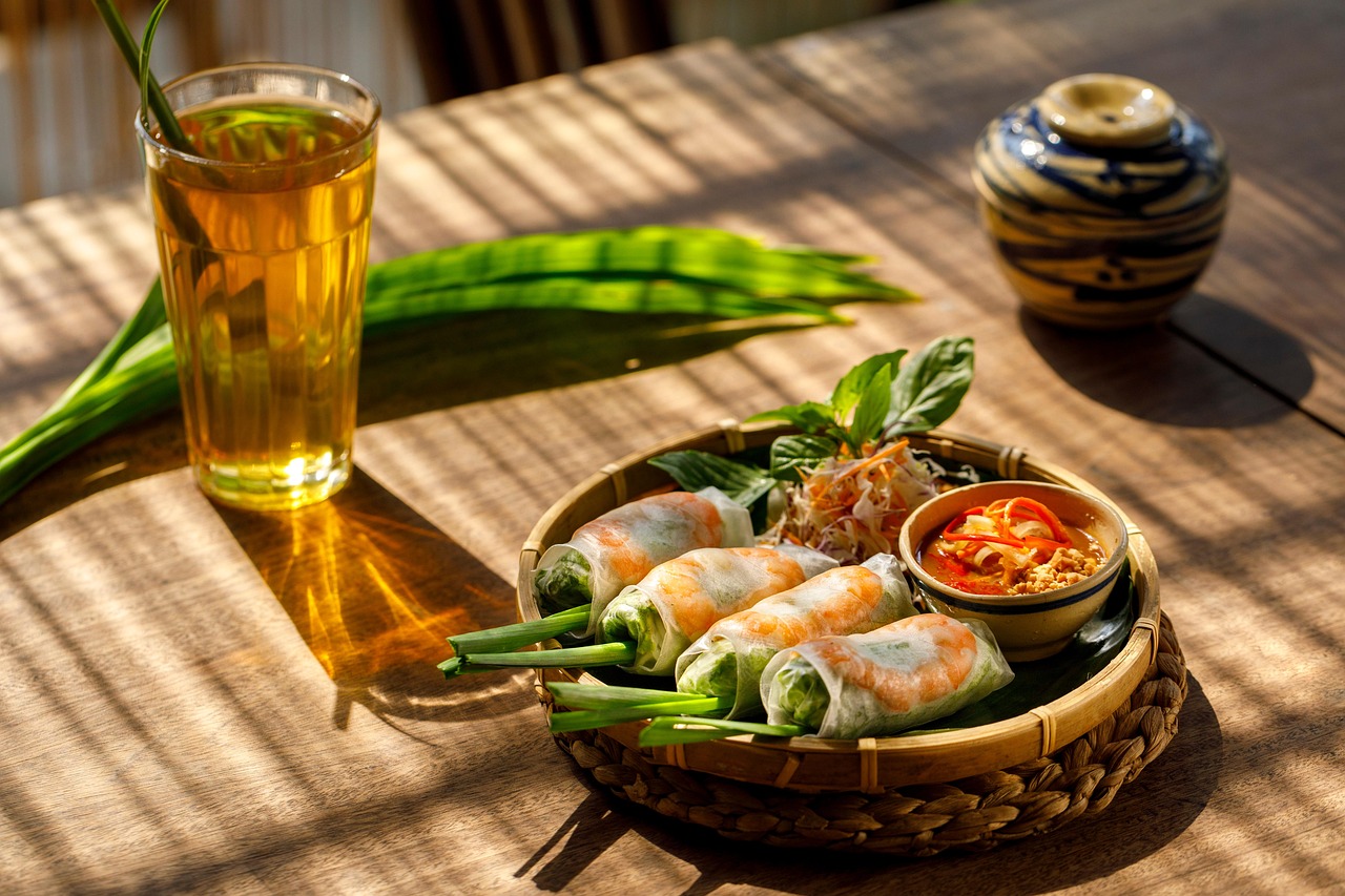 Traditional Vietnamese food served with dipping sauce and iced tea on a sunlit wooden table