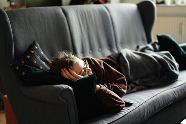 Person relaxing on a cozy couch with a blanket and TV remote during a lazy weekend movie marathon.
