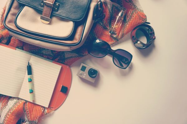 Flat lay of travel essentials including a notebook, sunglasses, action camera, watch, and a stylish bag, capturing the spirit of off-season trip planning.